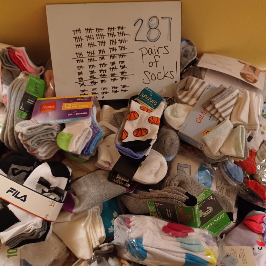 Large pile of new pairs of socks for children and youth with a small white board displaying the words "287 pairs of socks!" and 287 tally marks